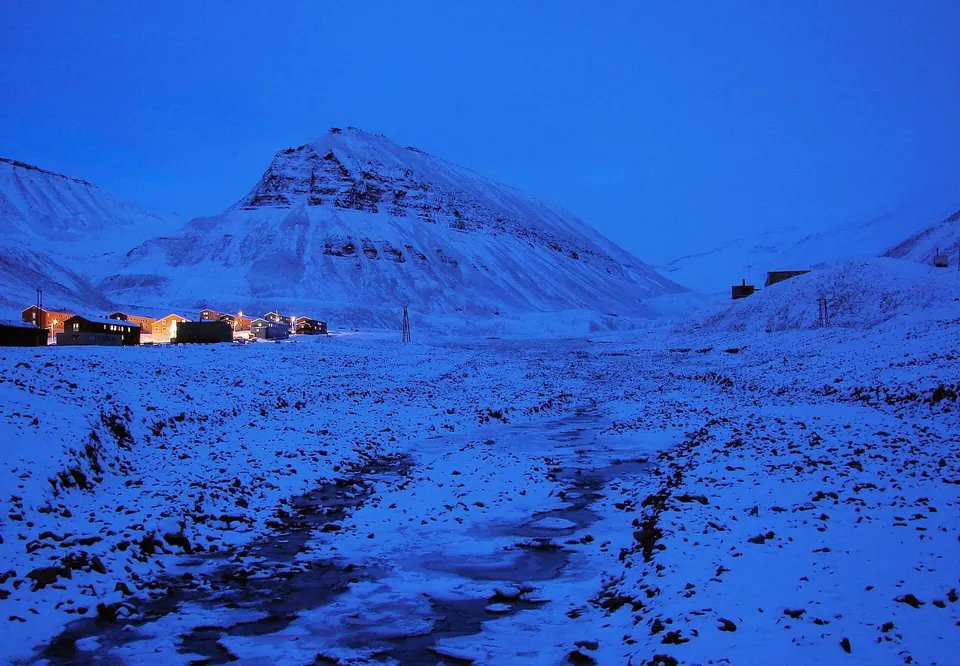 Longyearbyen talvivalossa, lumipeitteisiä tuntureita ja valaistuja taloja