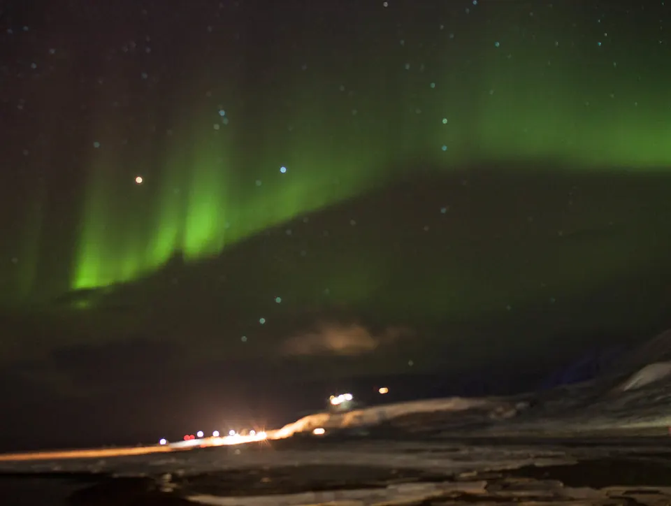 Norrsken över Svalbard med ljus från en väg
